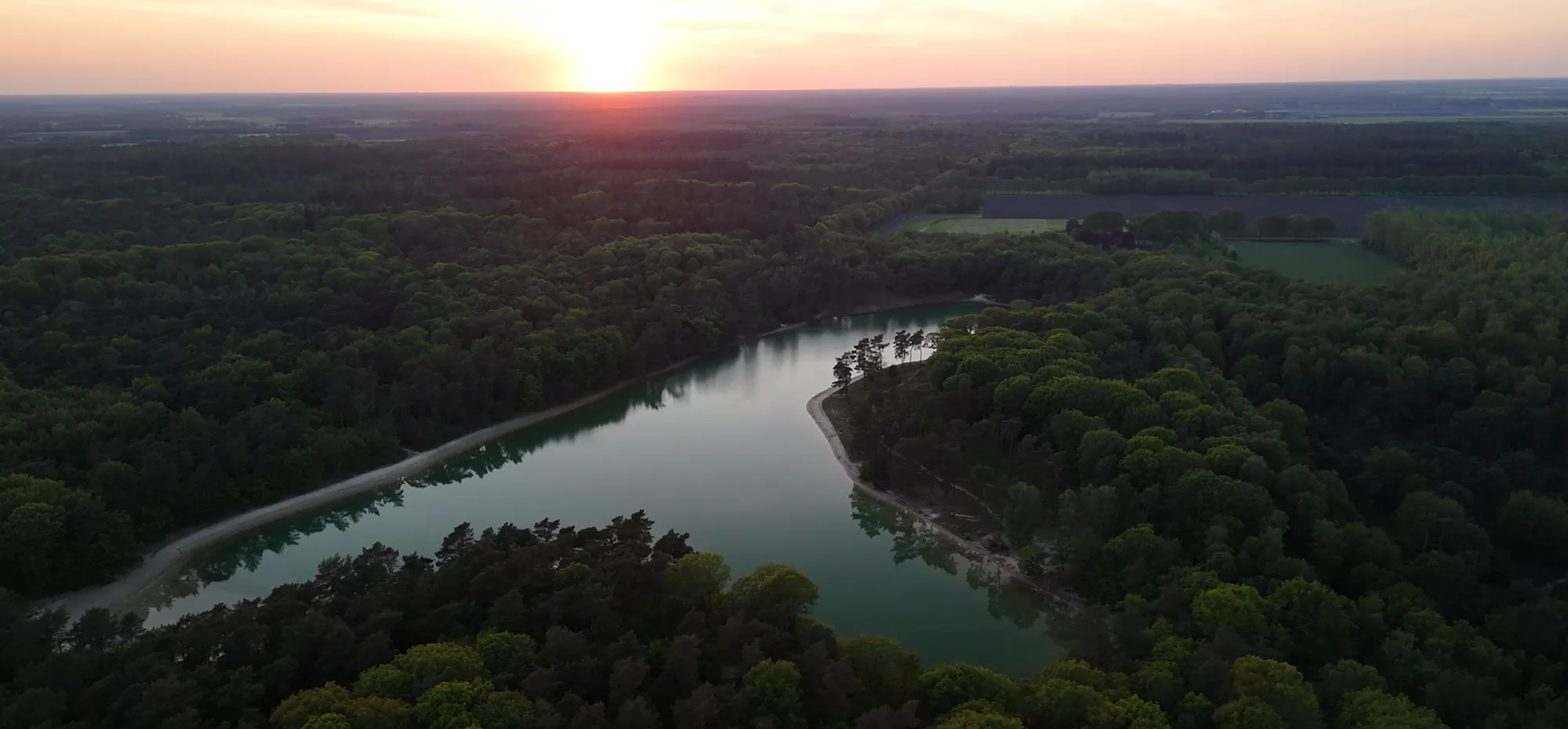 Zonsondergang boven een meer omringd door bos, vanuit de lucht