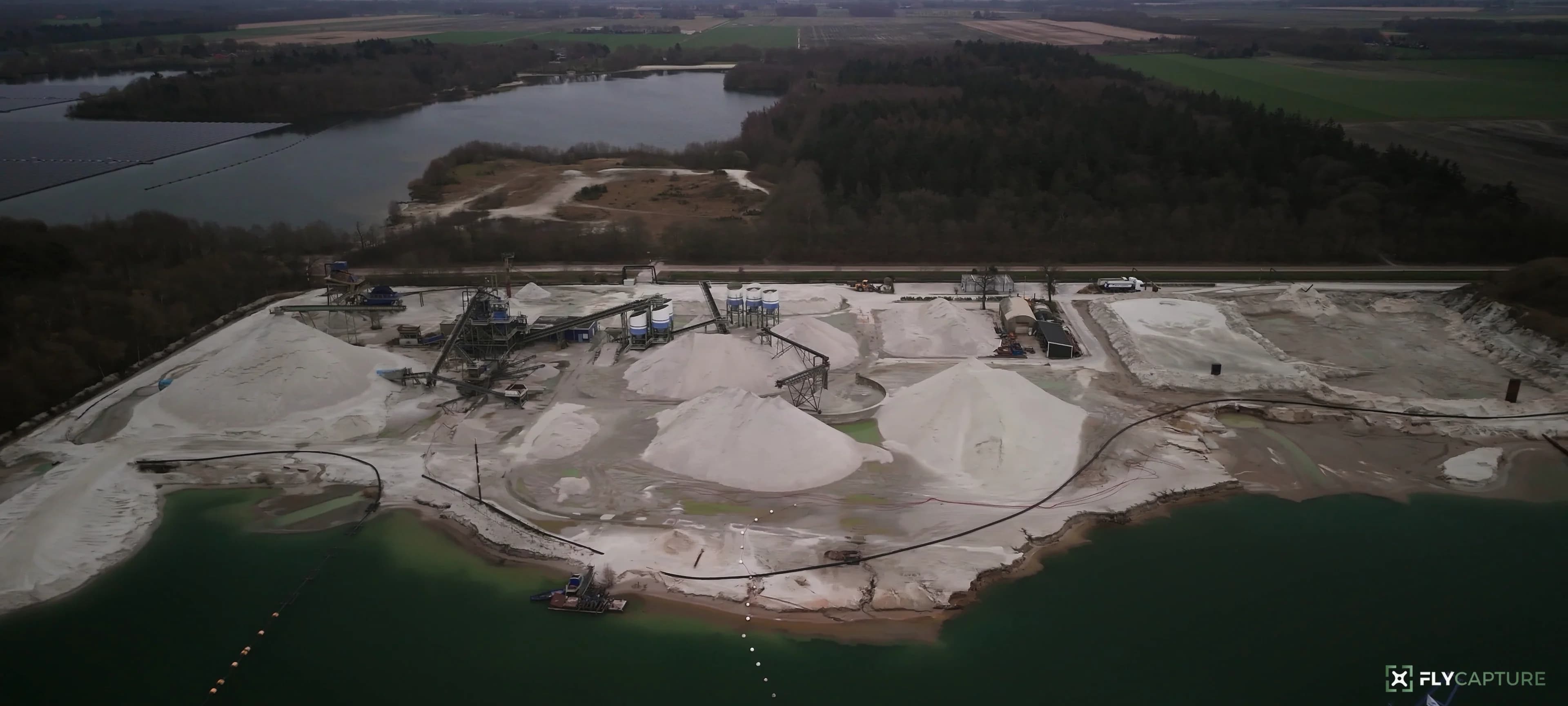 Overzicht van een zandwinning met depots aan het water