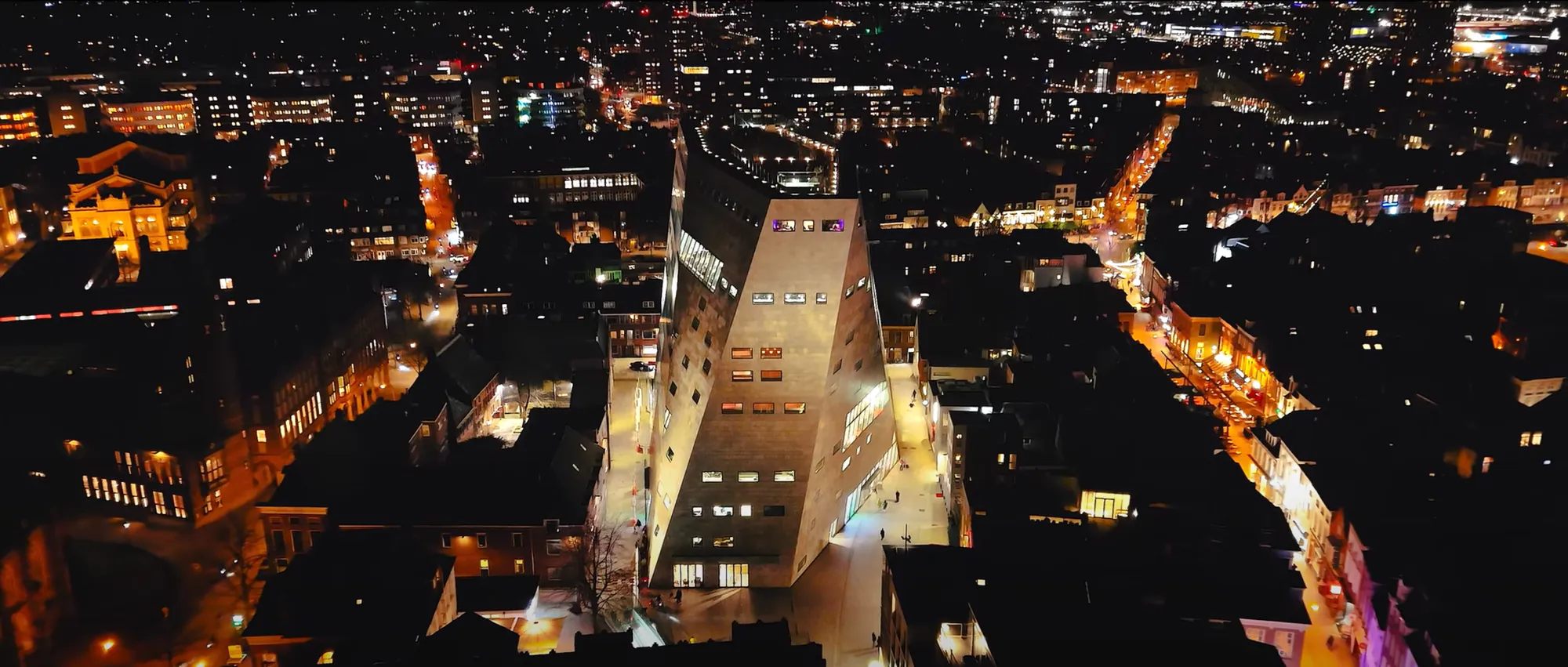 Dronebeeld bij nacht van een stadscentrum met een opvallend verlicht gebouw
