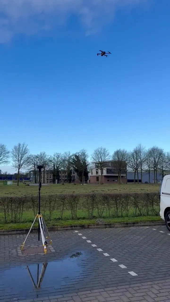 Drone in de lucht boven een terrein, met een GPS-meetstatief op de voorgrond